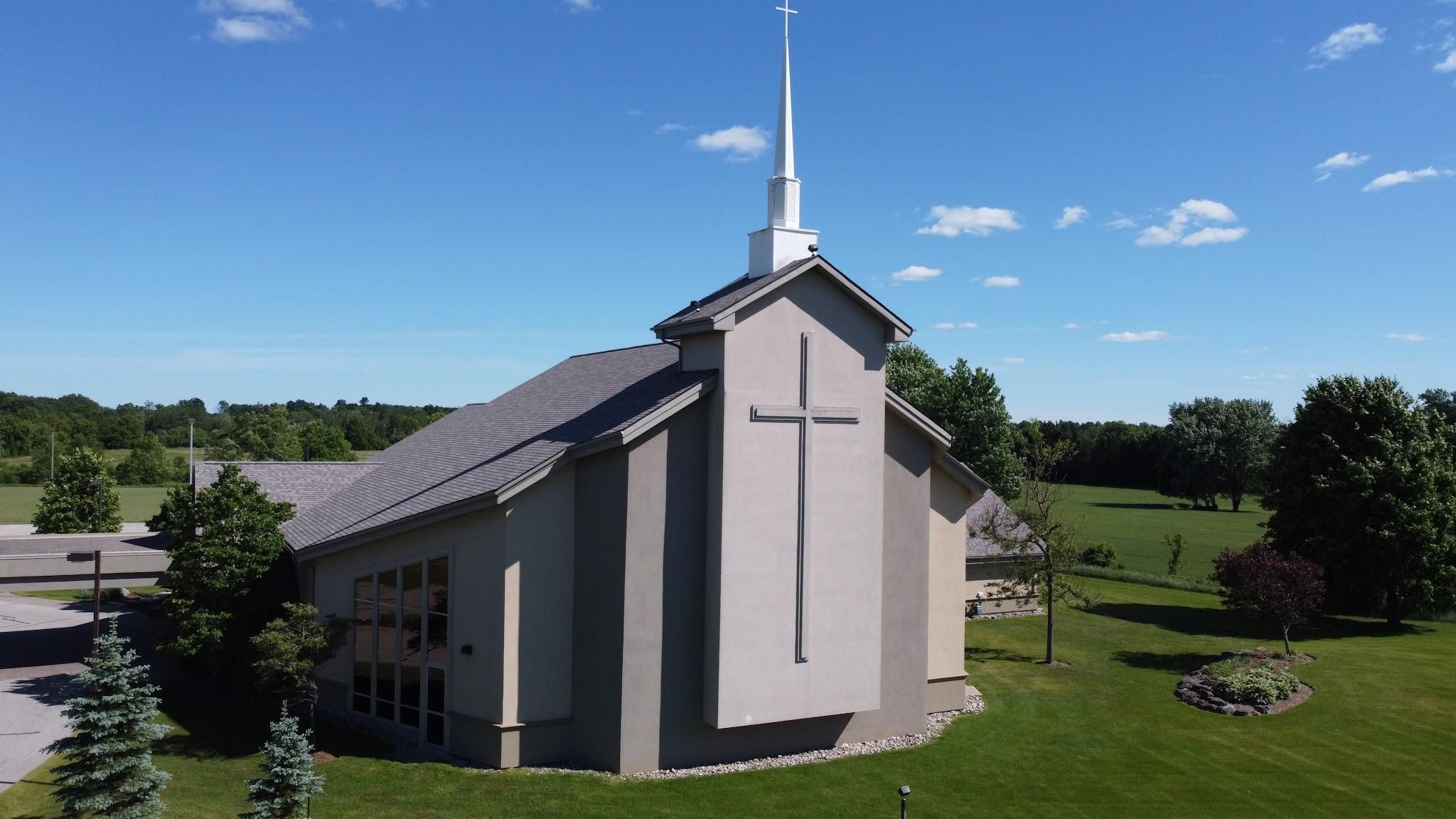 Emmanuel Canadian Reformed Church seen from above, a pale church with a tall white steeple and a wall of windows among fields